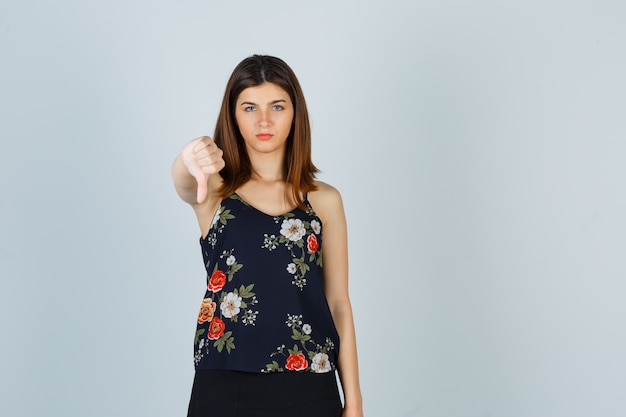 Portrait of beautiful young female showing thumb down in blouse