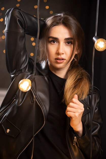 Portrait of a beautiful young model in black leather jacket posing near lamps.