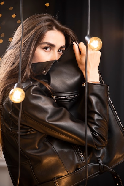 Portrait of a beautiful young model in black leather jacket posing near lamps.