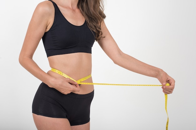 Free photo portrait of beautiful young woman measuring her figure size with tape measure