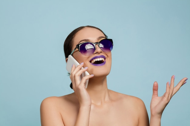 Portrait of beautiful young woman with bright make-up isolated on blue wall