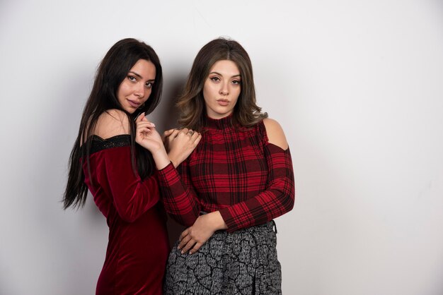 Portrait of beautiful young women looking at camera on white wall .