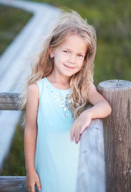 Portrait of blond cute teenage girl in a blue dress over outdoor natural field.