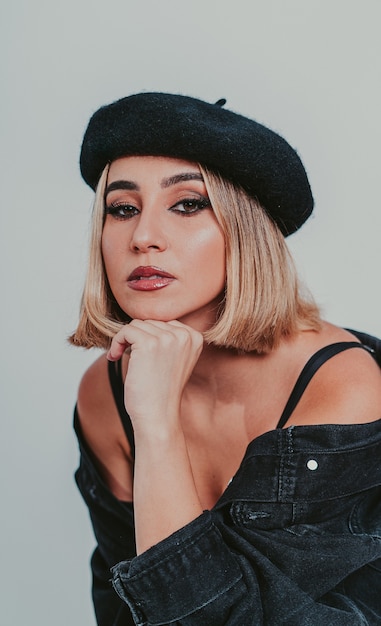 Free photo portrait of a blonde female wearing a beret and a black denim jacket against a gray wall