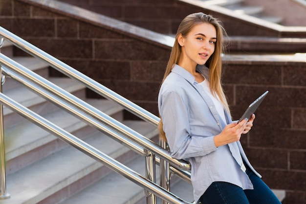 Portrait of blonde girl holding a tablet and looking at photographer