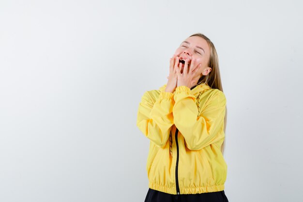 Portrait of blonde lady keeping hands on cheeks in tracksuit and looking blissful front view