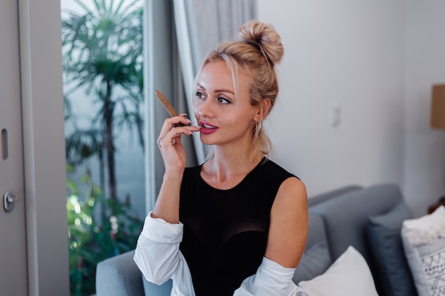 Portrait of blonde woman in body suit and white shirt with pink beautiful lips holding cigar