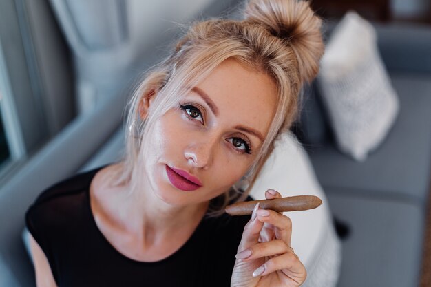 Portrait of blonde woman in body suit and white shirt with pink beautiful lips holding cigar