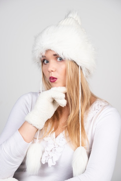 Portrait of blonde woman in winter outfit standing on gray wall.