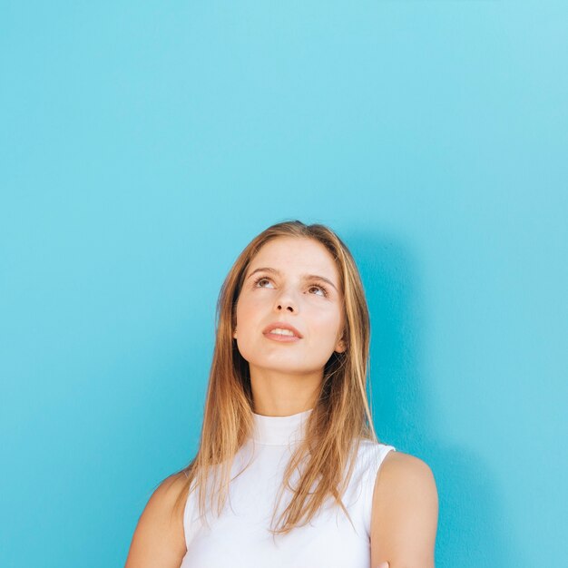 Portrait of a blonde young woman looking up against blue background