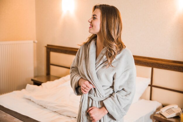 Portrait of a blonde young woman tying her bathrobe standing in the bedroom