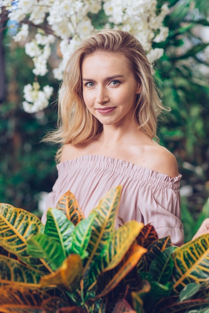 Free photo portrait of a blonde young woman with gray eyes standing in front of leaves