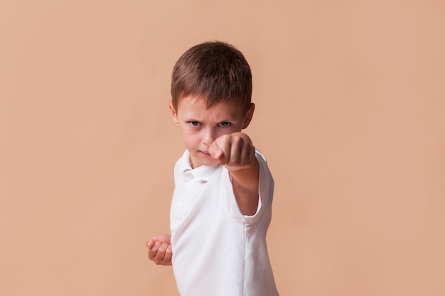 Portrait of boy clinching his fist for fighting on beige backdrop