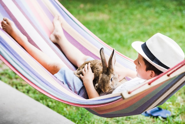 Free Photo portrait of boy lying on hammock with rabbit in hand