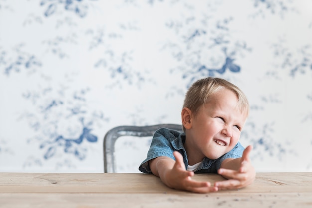 Portrait of a boy making funny face sitting in front of wallpaper