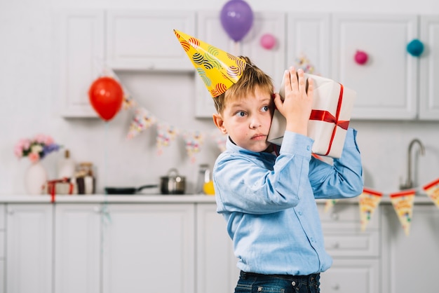 Free photo portrait of a boy shaking birthday gift in kitchen