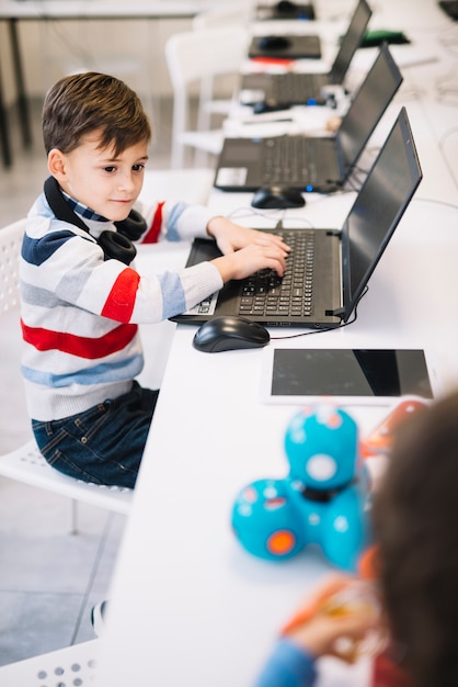 Free photo portrait of a boy using laptop looking at child playing with toy in the class