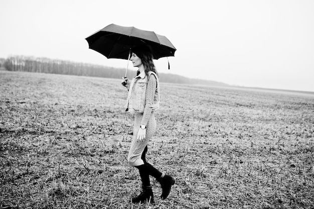 Free Photo portrait of brunette curly girl in jeans jacket with black umbrella at field