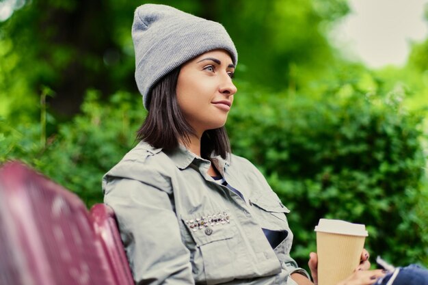 Free Photo portrait of brunette female in a hat drinks coffee in a summer park.