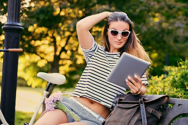 Free Photo portrait of brunette female using tablet pc with city bicycle in a park on background.