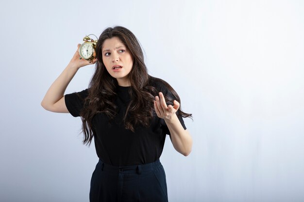 Portrait of brunette girl in black outfit holding clock and posing to camera. 