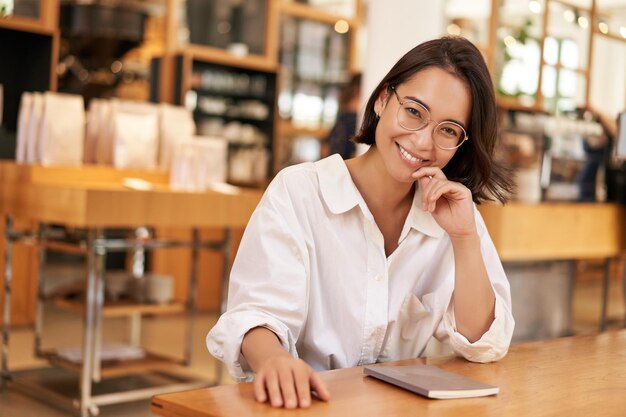 Portrait of brunette woman in cafe sitting with notebook working documents looking at camera and smi