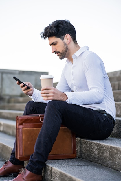 Portrait of a business man using his mobile phone while sitting on stairs outdoors