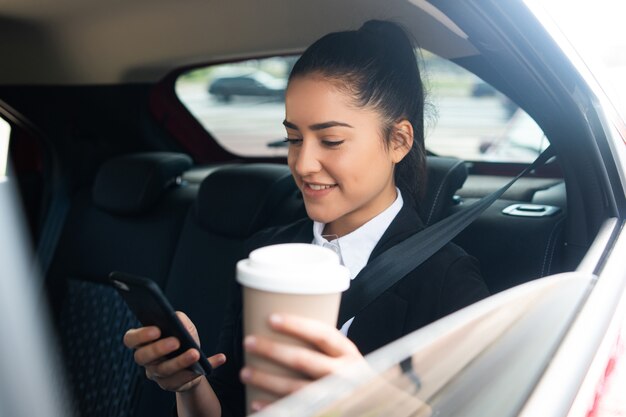 Portrait of business woman using her mobile phone on way to work in a car. Business concept.