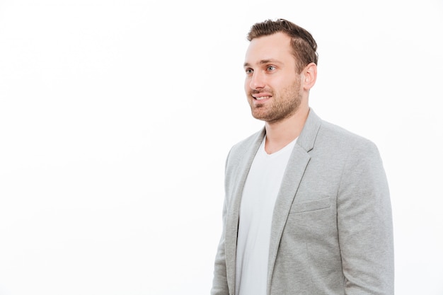 Portrait of businesslike guy in jacket having bristle posing with smile and looking aside, isolated over white wall copy space