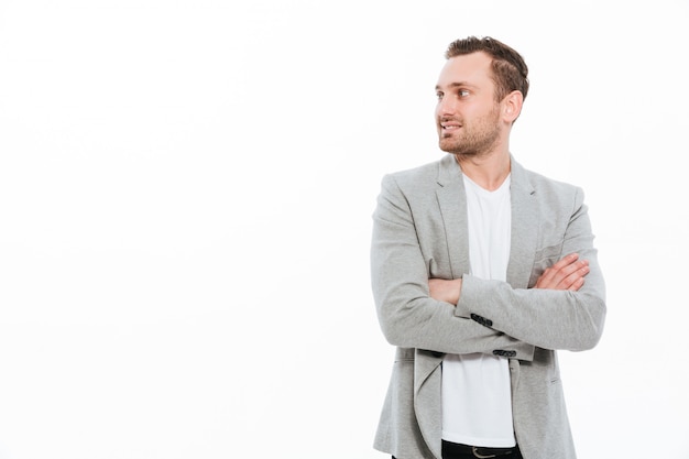 Free Photo portrait of businesslike man in jacket posing with broad smile keeping arms folded and looking aside, isolated over white wall copy space