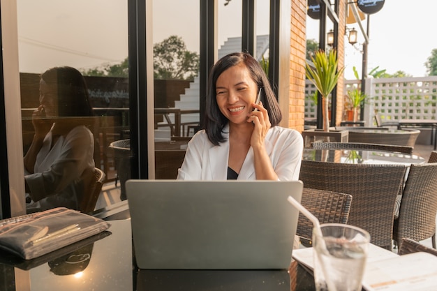 Portrait of businesswoman in a cafe using a laptop and talking with cellphone