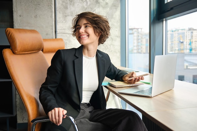 Free photo portrait of businesswoman manager talking to a coworker in an office sitting with laptop and