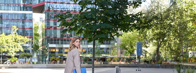 Free Photo portrait of businesswoman walking on street of an empty city center holding folder with work