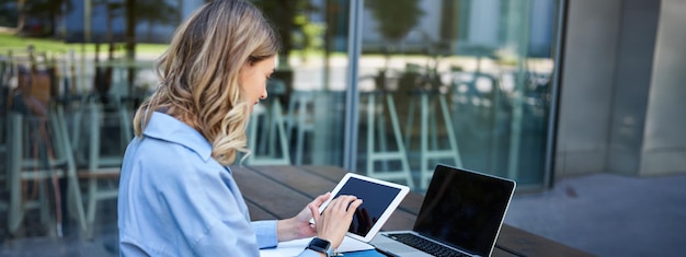 Free photo portrait of businesswoman working on digital tablet checking diagrams sitting outdoors on fresh air