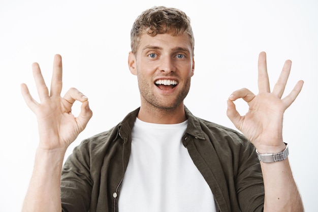 Portrait of carefree handsome blond man with bristle and blue eyes showing okay gestures and smiling satisfied