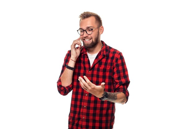 Portrait of a casual young man speaking on the phone and smiling while looking away, somewhere up. Studio shot. Young hipster man in checkered shirt and glasses wearing on white background