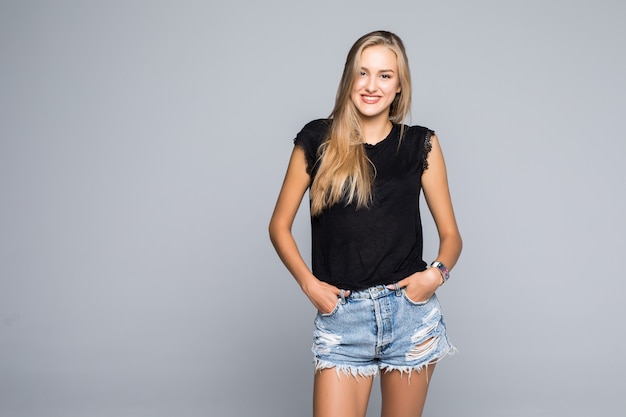 Portrait of a casual young woman holding her thumbs in the loops of her short jeans while smiling for the camera on a gray backgroud