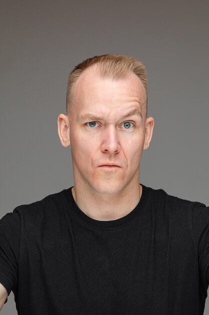 Portrait of caucasian man in black t-shirt with a doubt isolated on grey wall