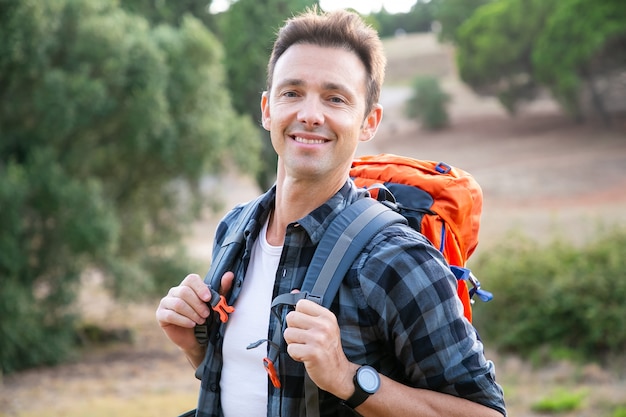 Free photo portrait of caucasian man standing, smiling. happy hiker enjoying nature, carrying backpacks and posing. tourism, adventure and summer vacation concept