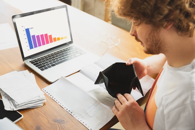 Portrait of caucasian unset and despair man watching financial and economical graphs during coronavirus quarantine, problems