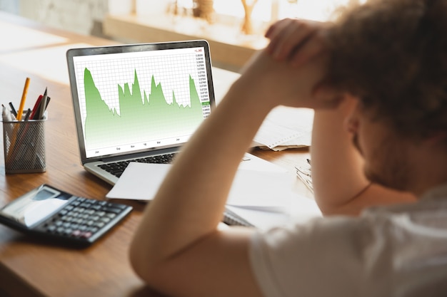 Portrait of caucasian unset and despair man watching financial and economical graphs during coronavirus quarantine, problems