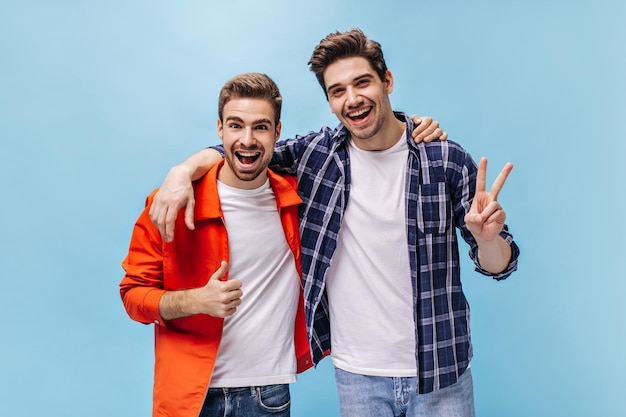 Portrait of charming brunet men in white tshirts and jeans on isolated Man in orange jacket show thump up and guy in checkered shirt show peace sign