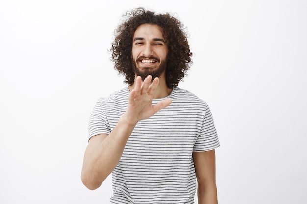 Portrait of charming carefree hispanic boyfriend with curly hair and beard, waving palm in no thanks or stop gesture and smiling broadly with friendly attitude