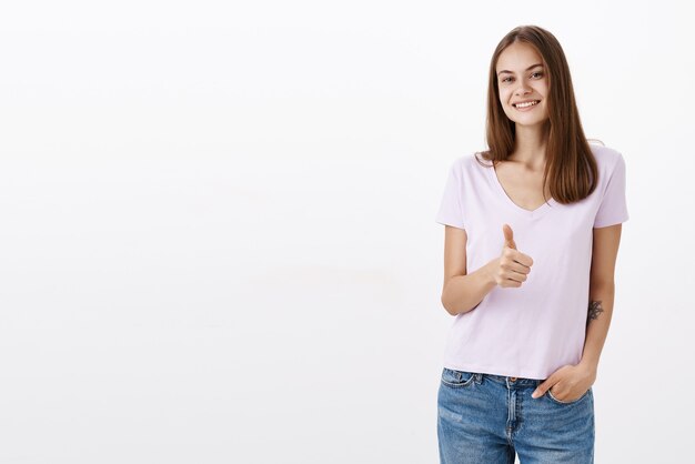 Portrait of charming friendly-looking confident and happy woman with brown hair and tattoo holding hand in pocket casually smiling assured and showing thumb up