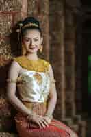 Free photo portrait charming thai woman in beautiful traditional dress costume, woman wearing typical thai dress sitting in archaeological site or thai temple, identity culture of thailand