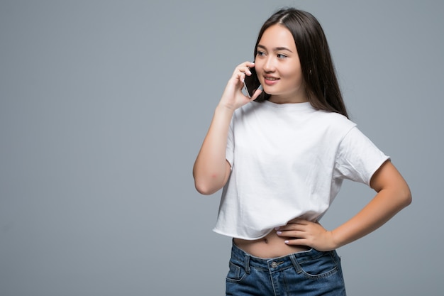 Portrait of a cheerful asian woman talking on mobile phone and looking away over gray background