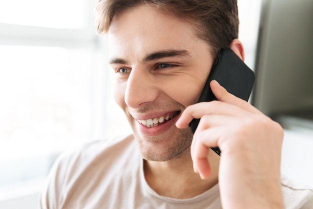 Portrait of cheerful attractive man talking on phone at home