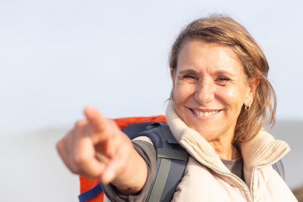 Free photo portrait of cheerful elderly woman with backpack. sporty woman in casual clothes smiling and pointing. sport, adventure, hobby concept