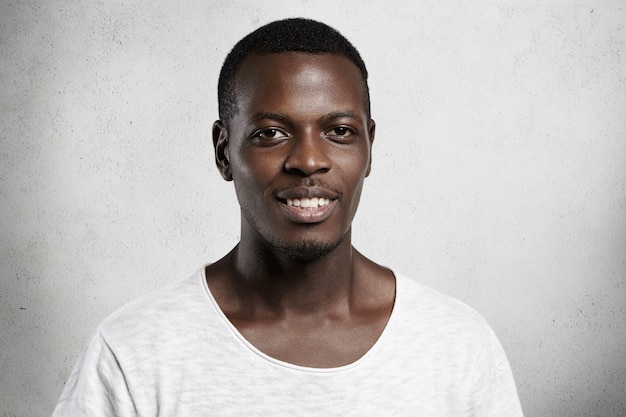 Portrait of cheerful good-looking African model wearing casual t-shirt  with happy smile, showing his white perfect teeth, joyful with some pleasant news, having rest indoors