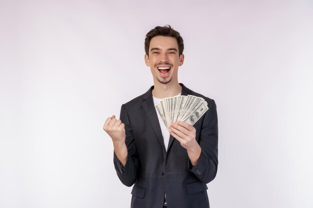 Portrait of a cheerful man holding dollar bills and doing winner gesture clenching fist over white background